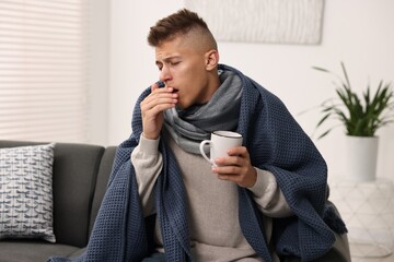 Cold symptom. Young man with hot tea coughing at home