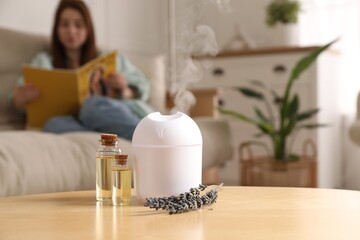 Woman reading magazine at home, focus on aroma diffuser, bottles of essential oils and lavender...