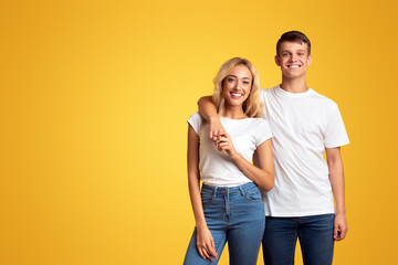 Young and beautiful. Portrait of happy millennial couple cuddling on yellow studio background, free space