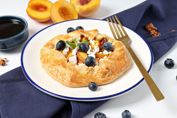Fruit galette on plate, towel, fruit and jam on white background, close up