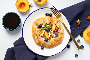 Fruit galette on plate, towel, fruit and jam on white background, top view
