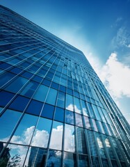 Obraz premium A tall glass skyscraper reflects the bright blue sky and puffy clouds