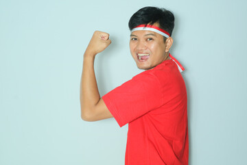 Indonesian man showing his arm muscle with enthusiastic expression. Wearing a red t-shirt