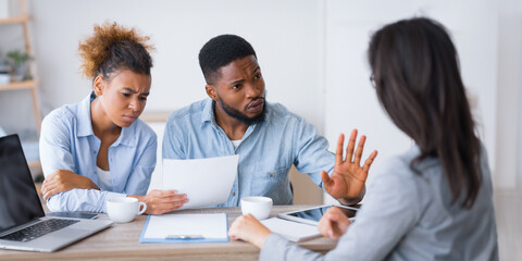 Angry afro couple criticizing and rejecting insurance broker's advice sitting at her office. Selective focus