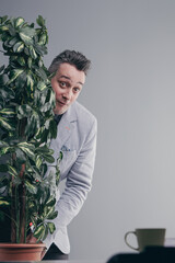 Businessman hiding behind plant having bad unprofessional behavi