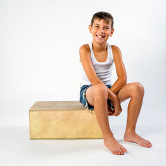 Cute smiling preteen boy in cut off jean shorts and a tank top, sitting on a crate