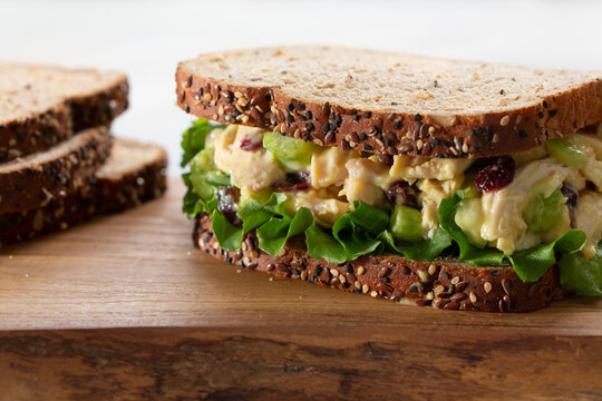 Honey Mustard Rotisserie Chicken Salad  on multigrain bread with dried cranberries, celery and lettuce on a wooden cutting board