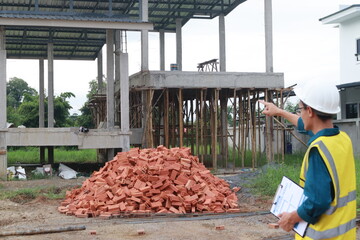 A male engineer at a construction site wears a hardhat and reflective clothing, reviewing blueprints. He coordinates with a team, safety and efficient project development in construction industry.