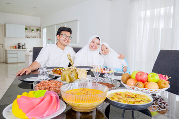 Muslim parents and their daughter smiling at the camera while having dinner together during Eid Mubarak in dining room at home