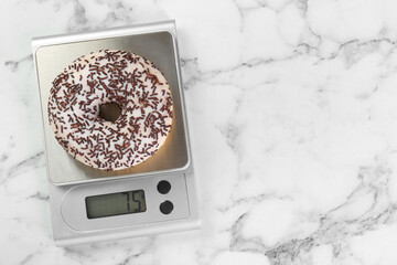 Kitchen scale with donut on white marble table, top view. Space for text