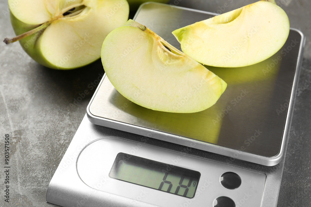 Poster Kitchen scale with pieces of apple and fruits on grey textured table, closeup