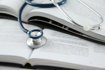 One medical stethoscope and books on white table, closeup