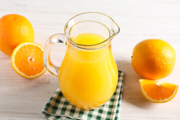 Tasty orange juice in glass jug and fresh fruits on white wooden table