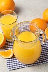Tasty orange juice in jug, glass and citrus fruits on light table
