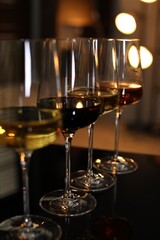 Different tasty wines in glasses on table against blurred lights, closeup