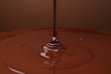 Pouring delicious melted chocolate on brown background, closeup