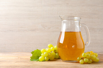 Tasty juice in glass jug and fresh grapes on wooden table, space for text