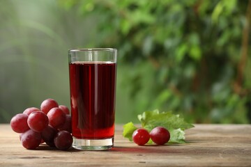 Tasty juice in glass, fresh grapes and leaf on wooden table. Space for text