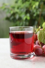 Tasty grape juice in glass, leaf and berries on light textured table against blurred green background, closeup