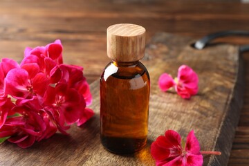 Geranium essential oil in bottle and beautiful flowers on wooden table