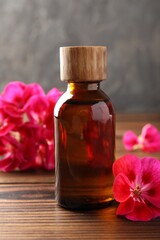 Geranium essential oil in bottle and beautiful flowers on wooden table