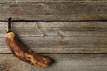 Overripe banana with dark spots on wooden table, top view. Space for text