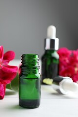 Bottles of geranium essential oil and beautiful flowers on white wooden table, closeup