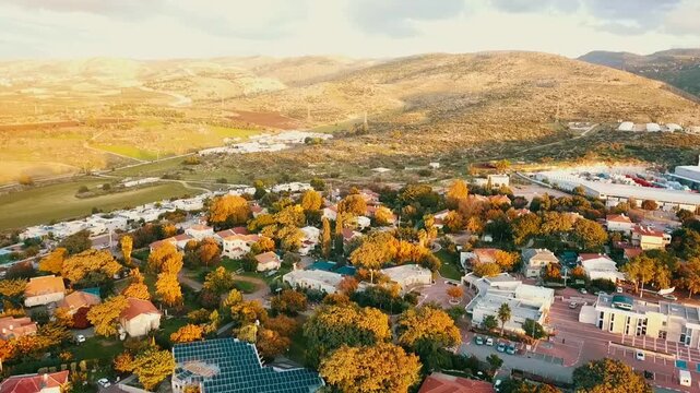Drone footage captures the picturesque Mevo Horon settlement nestled among rolling hills. Autumn colors paint the landscape as golden light bathes the community, showcasing Israel's diverse topography