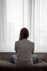 Depressed woman: sitting, hugging her knees, head down, face hidden by hair, expression of despair and sadness, dim lighting emphasizes gloomy © daniiD