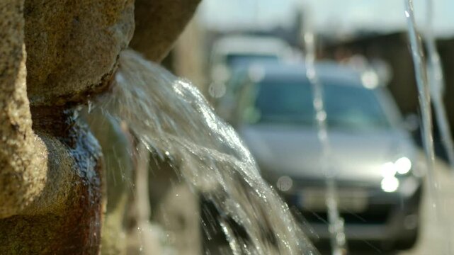 Water pouring out of a fountain with a car in the background.