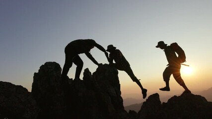 Silhouettes a group of  climbing on mountain and helping. Help and assistance concept.  person hiking help teamwork and trust.