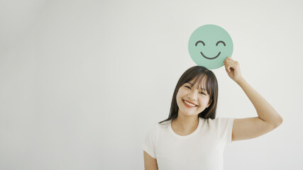 Happy young Asian woman holding smile emoji face, positive mental health, world mental health day concept