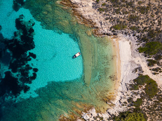 Aerial view of a secluded cove in Sithonia, Greece, with crystal-clear turquoise waters, rocky coastline, and a small boat anchored near the shore, capturing the pristine beauty of the Mediterranean