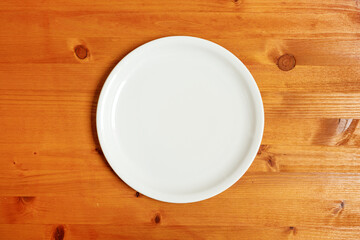Empty white dinner plate on wooden table from above as mockup copy space