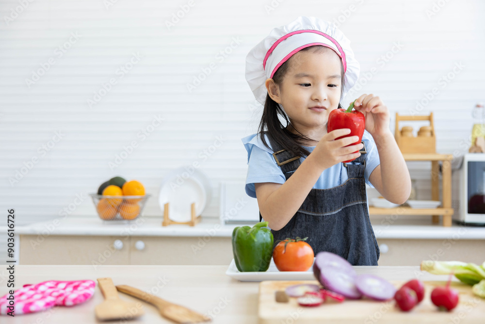 Wall mural asian kid holding bell pepper and preparing vegetables meal in the kitchen