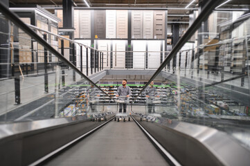 A man with a shopping cart on an escalator in a hardware store.