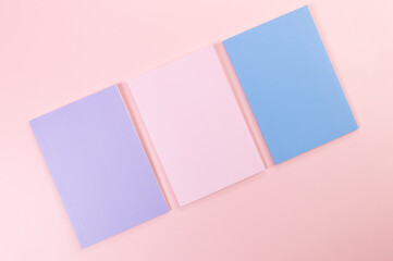 Top view of pink, purple and blue notebooks on pink background. School, office wallpaper. Flat lay, copy space.
