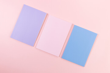 Top view of pink, purple and blue notebooks on pink background. School, office wallpaper. Flat lay, copy space.