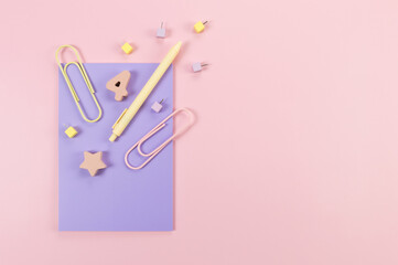 Top view of purple notebook on pink background. Paperclips, pen, number, shape and pins. School, office wallpaper. Flat lay, copy space.