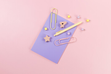 Top view of purple notebook on pink background. Paperclips, pen, number, shape and pins. School, office wallpaper. Flat lay, copy space.