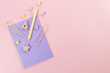 Top view of purple notebook on pink background. Paperclips, pen, number, shape and pins. School, office wallpaper. Flat lay, copy space.