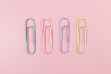 Top view of colorful paperclips on pink background. School, office wallpaper. Flat lay, copy space.