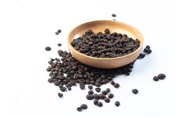 Coffee beans in a wooden bowl and some coffee beans lie below on a white background