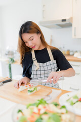 Young asian woman using tongs to taking tomatoes on the bread and making delicious sandwich for healthy breakfast food to preparing homemade snack in modern kitchen with healthy lifestyle at home