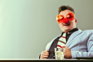 Businessman wearing clown nose and glasses drinking alcohol