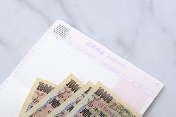 テーブルの上に開いた状態で置かれた銀行の預金通帳と、1万円札
