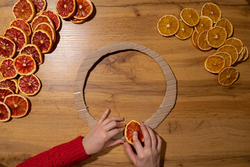 Step by step instruction of making handmade Christmas wreath made of dry fruits oranges and grapefruits. Female hands creating craft homemade decor. New year celebration. Winter holidays