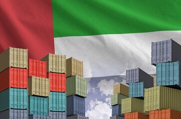 United Arab Emirates flag and big stack of shipping cargo containers in docks with sky background...