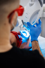 Patient whitens his teeth wearing goggles and lip retractor. Dental whitening procedure by...