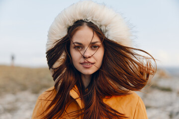 Woman in orange coat enjoying a breezy day at the beach, traveling in style and embracing nature's beauty